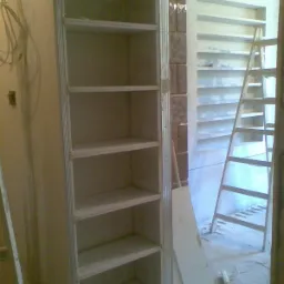 Montaż szkieletu szafy wnękowej z płyt kartonowo-gipsowych, widoczna drabina i fragment ściany z dekoracyjną cegłą.